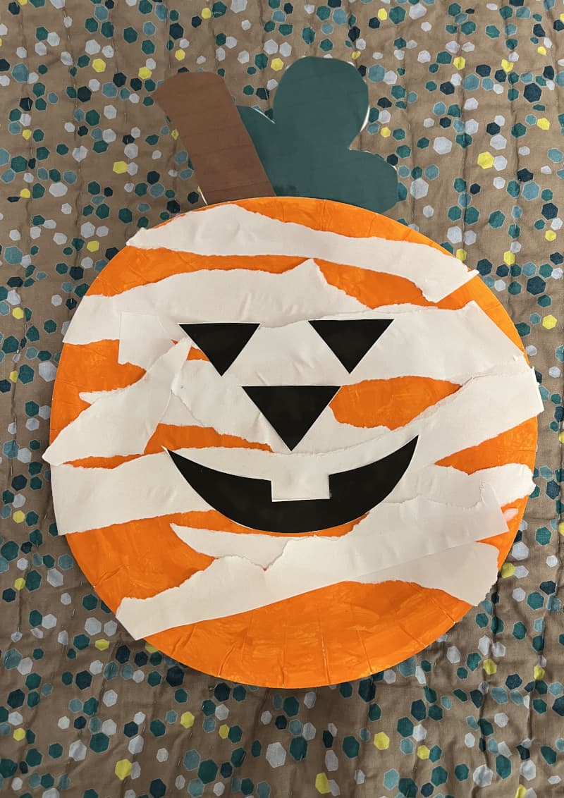 Κολοκύθα Halloween φτιαγμένη από χάρτινο πιάτο βαμμένο πορτοκαλί με χαρακτηριστικά από λωρίδες χαρτιού