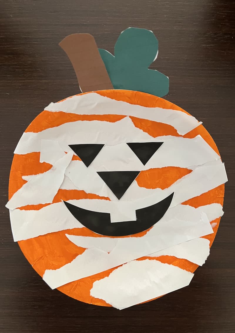 Κολοκύθα Halloween φτιαγμένη από χάρτινο πιάτο βαμμένο πορτοκαλί με χαρακτηριστικά από λωρίδες χαρτιού