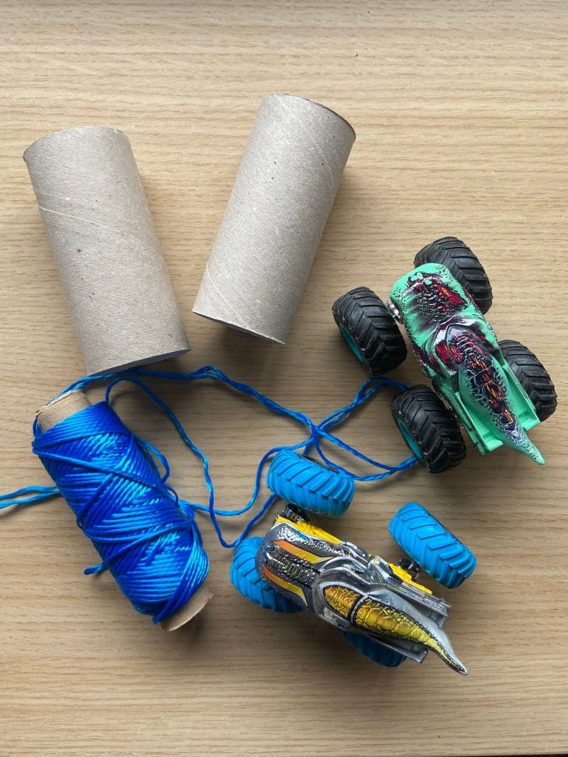 Educational game for toddlers with toy cars, rope, toilet paper roll.