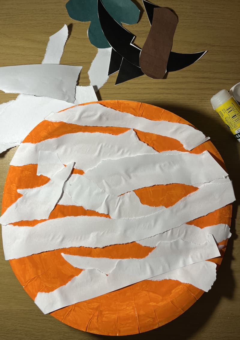 Κολοκύθα Halloween φτιαγμένη από χάρτινο πιάτο βαμμένο πορτοκαλί με χαρακτηριστικά από λωρίδες χαρτιού